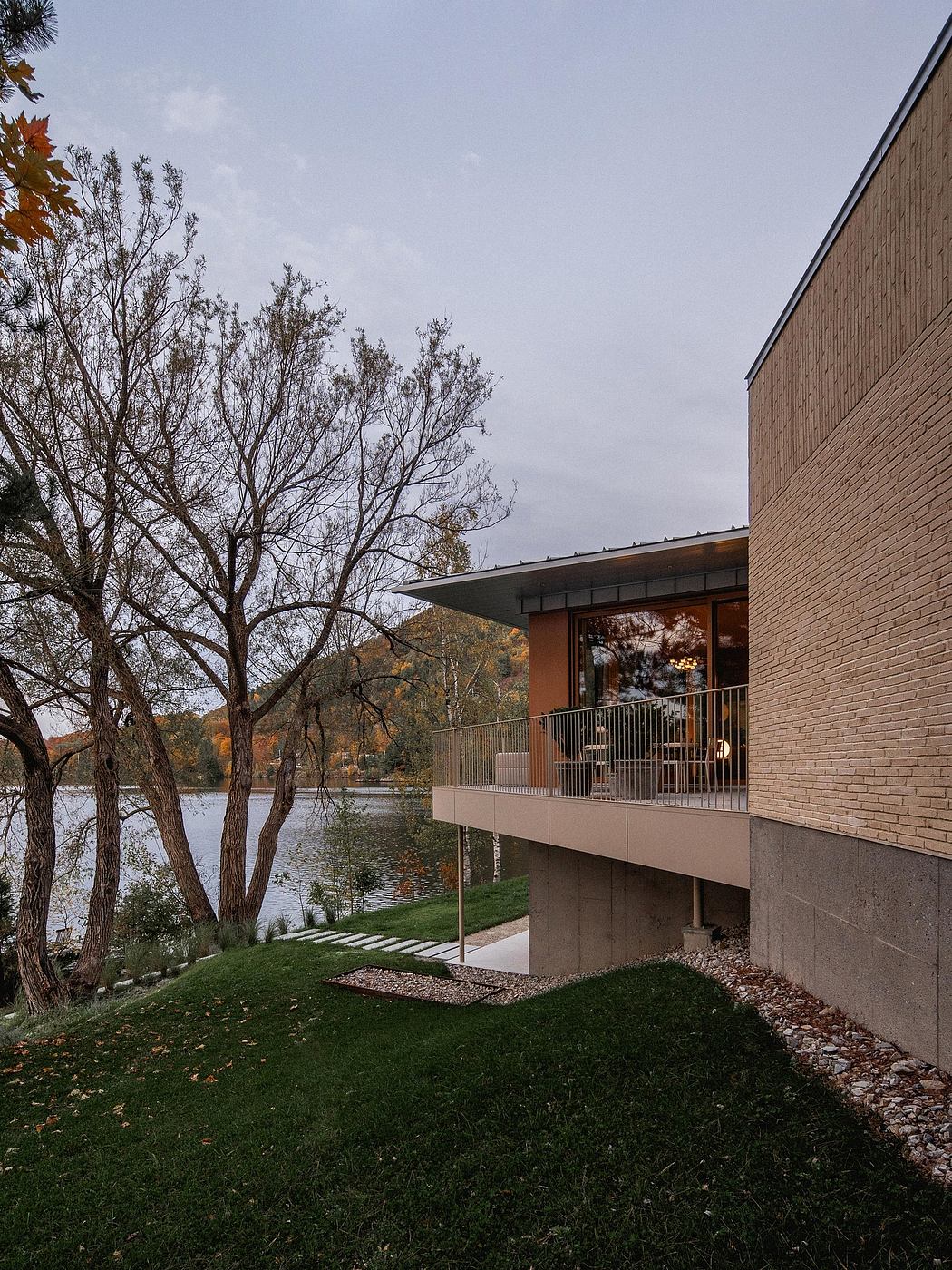 A contemporary brick building with a balcony overlooking a lake and fall foliage.