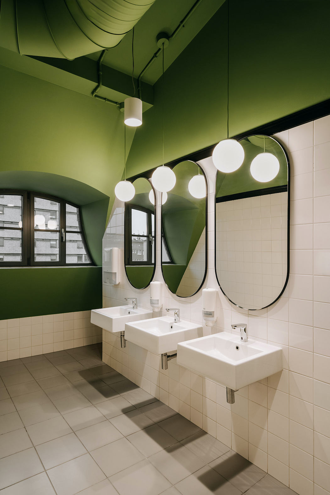 Sleek, modern bathroom with curved mirrors, pendant lights, and white tile walls.