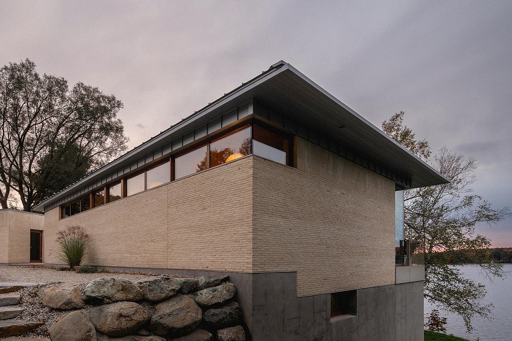 Modern architectural design featuring clean lines, brick exterior, and large windows overlooking a lake.