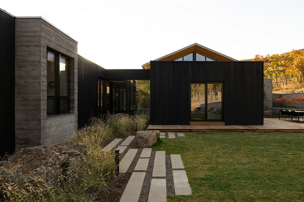 A modern, minimalist house with clean lines, large windows, and a wooden deck overlooking greenery.