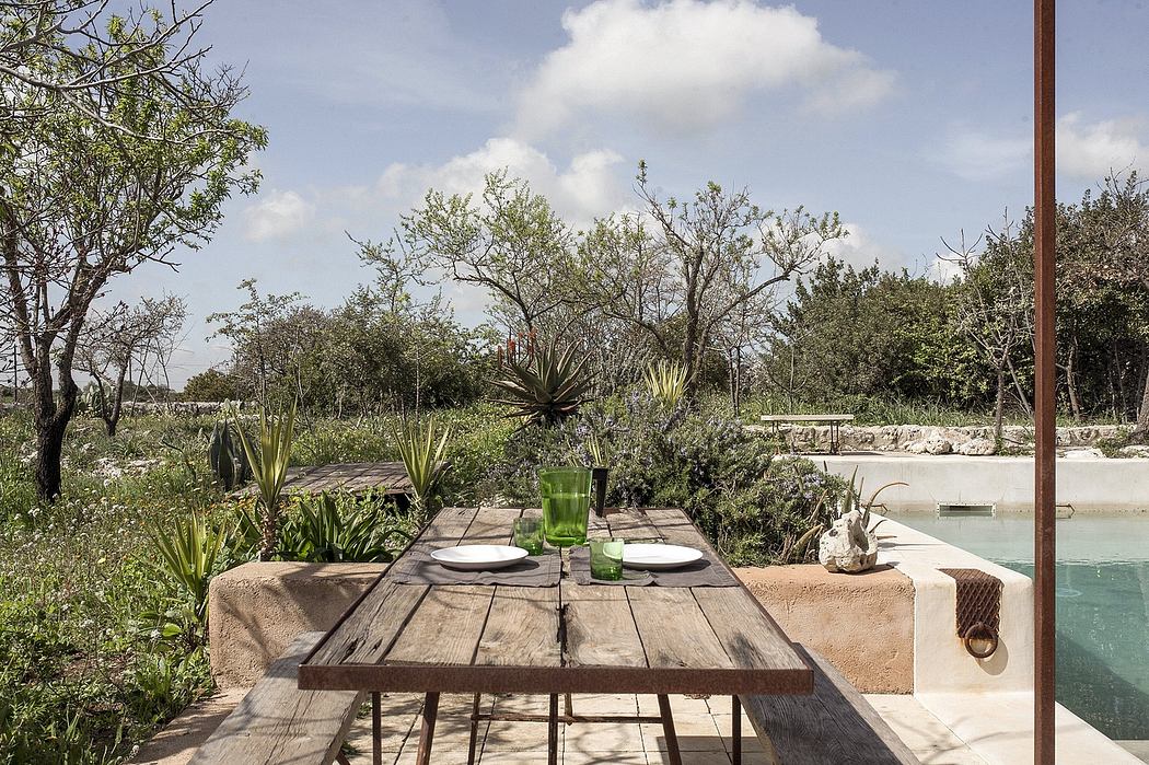 Outdoor dining area with rustic table, lush vegetation, and a pool amid a natural setting.