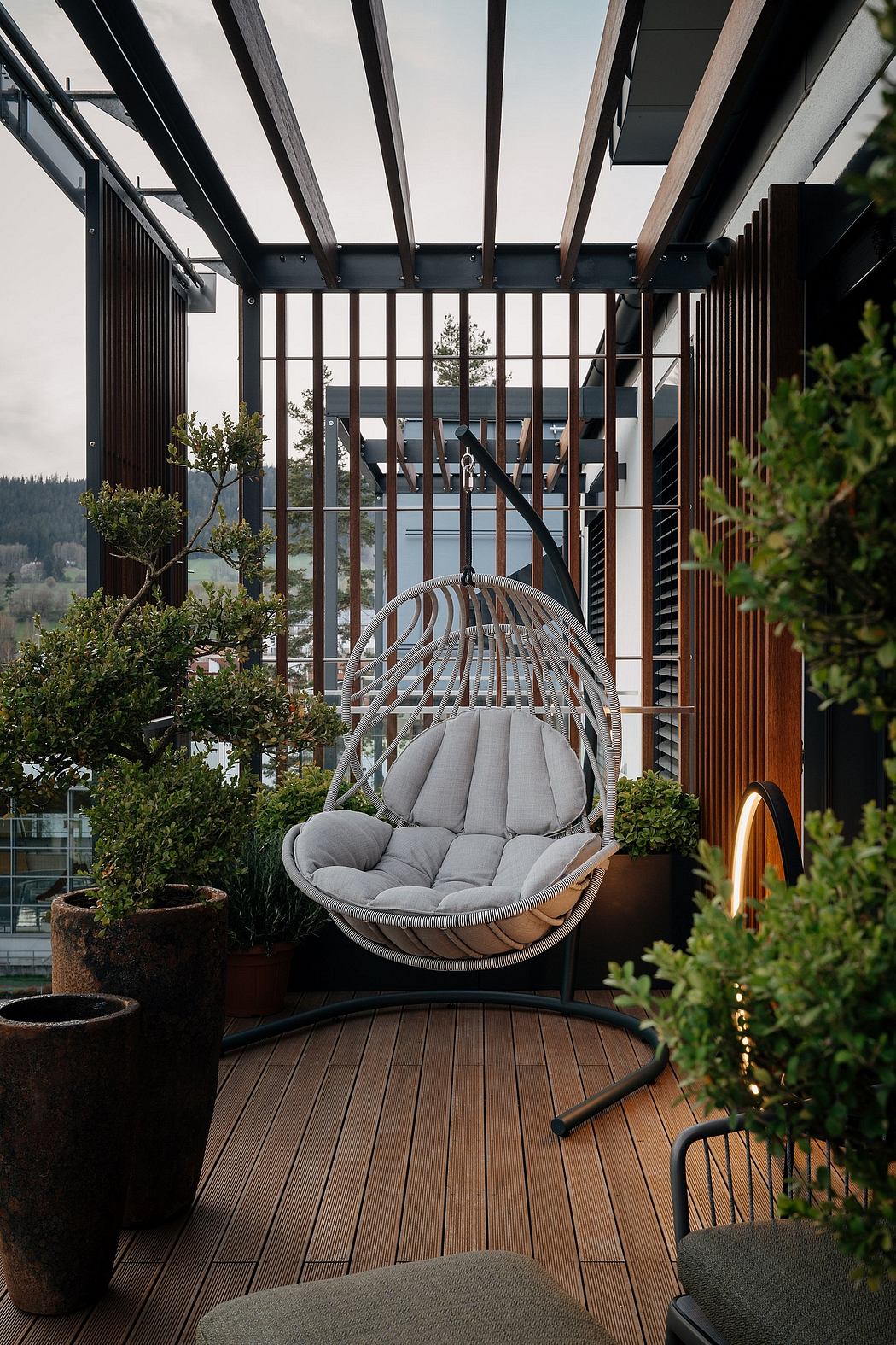 Cozy outdoor seating area with rattan swing chair, wooden deck, and glass-walled structure.