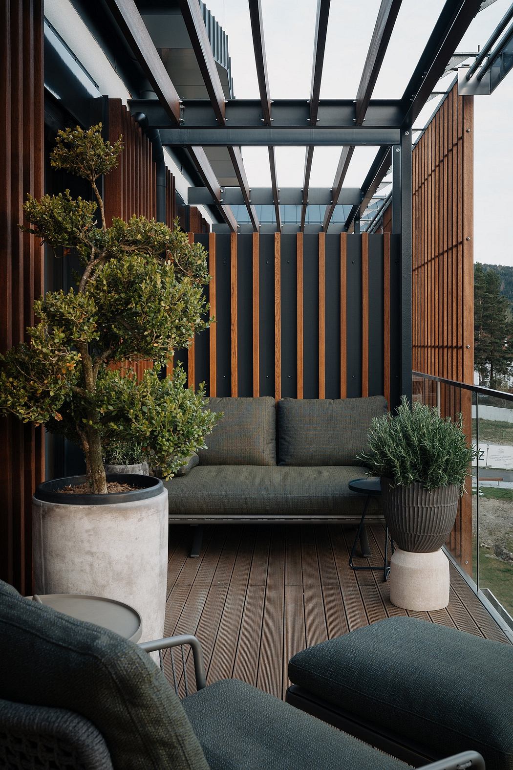 Sleek outdoor seating space with wooden beams, glass panels, and potted greenery.