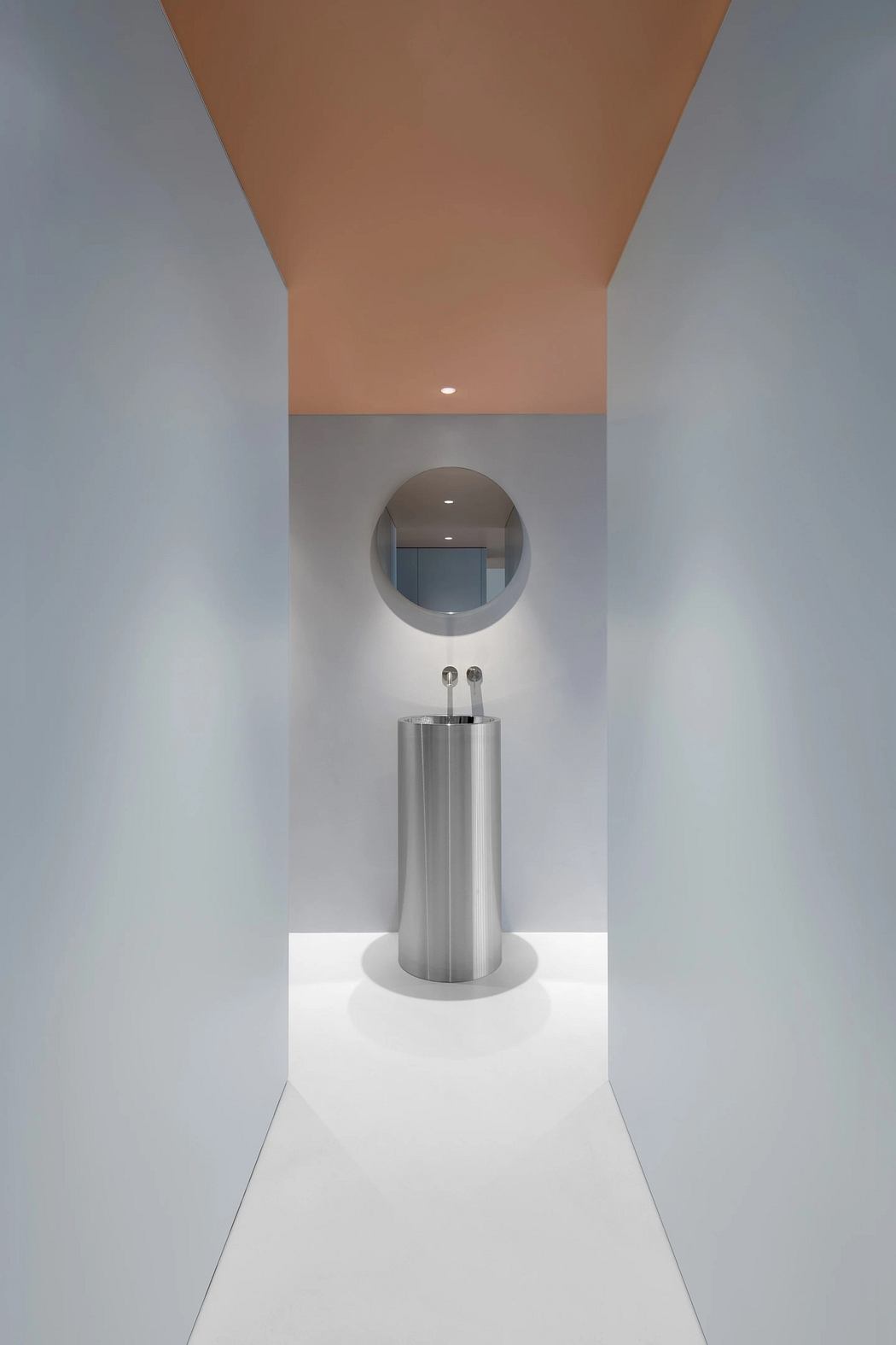 Minimalist bathroom design featuring a round mirror and a stainless steel pedestal sink.