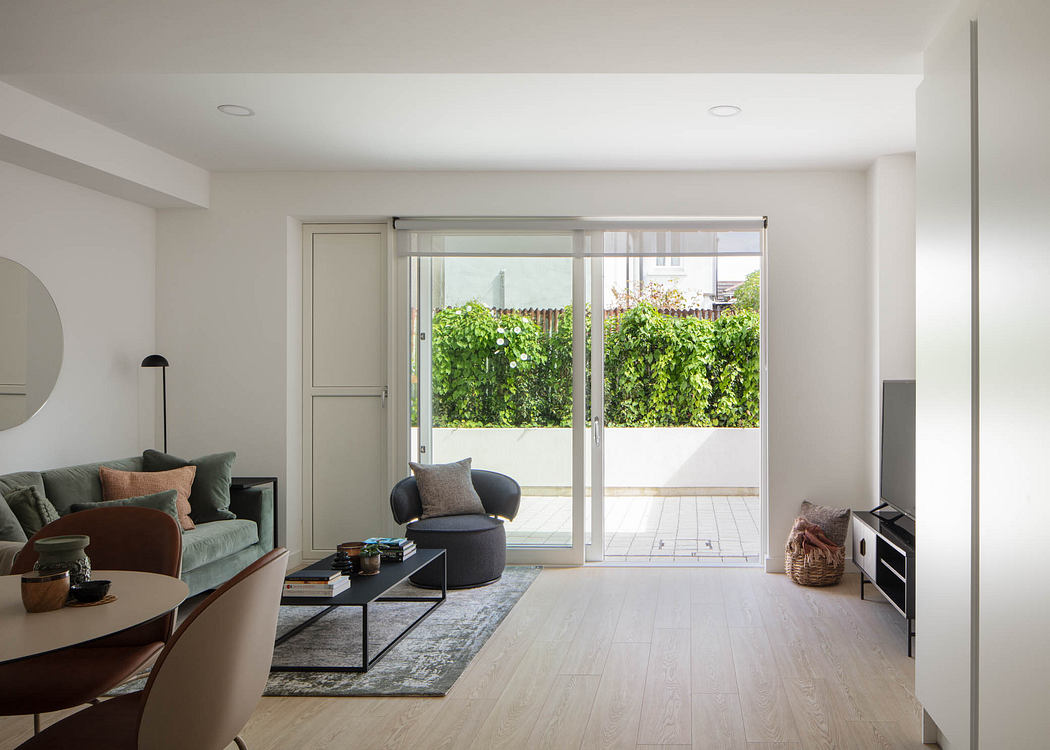 Minimalist living room with large windows, modern furniture, and lush greenery outside.