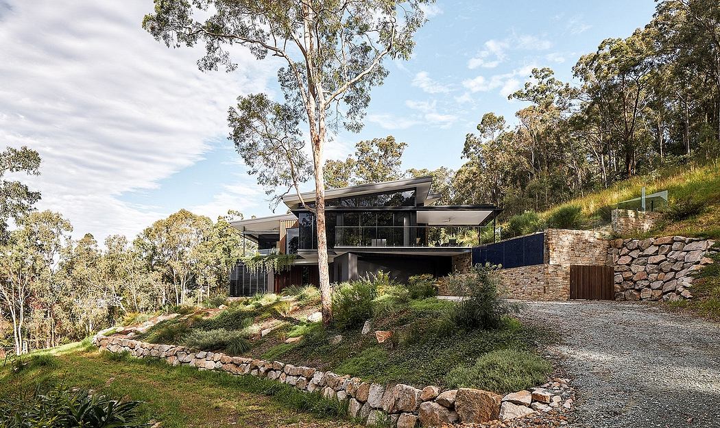 A modern, architecturally-designed home nestled among trees, with stone walls and glass panels.