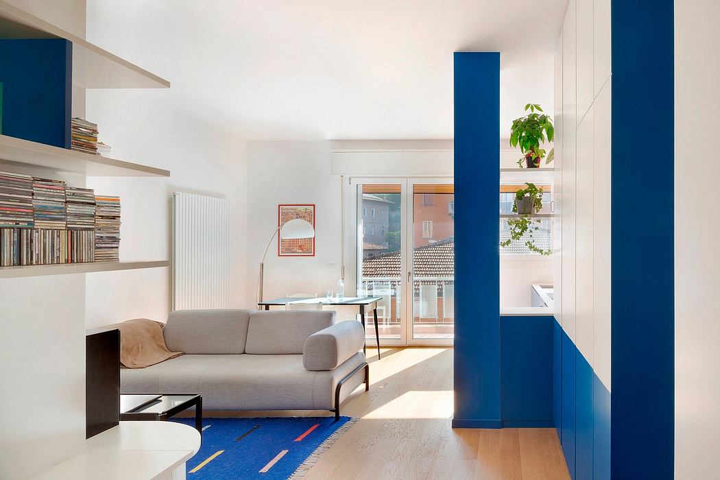 Minimalist living room with white walls, wooden floors, blue cabinetry, and a cozy sofa.