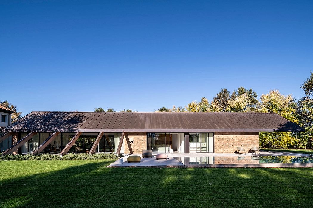 A contemporary brick and glass house with a sloped metal roof and open porch overlooking a grassy yard.