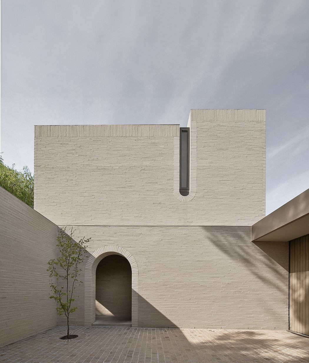 Minimalist architectural design with brick facade, arched entrance, and recessed window.