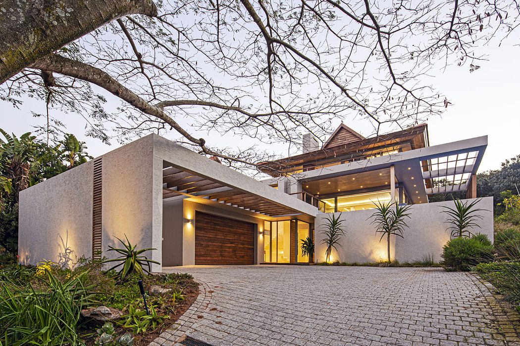 Modern luxury home with sleek, minimalist architecture, warm lighting, and lush landscaping.