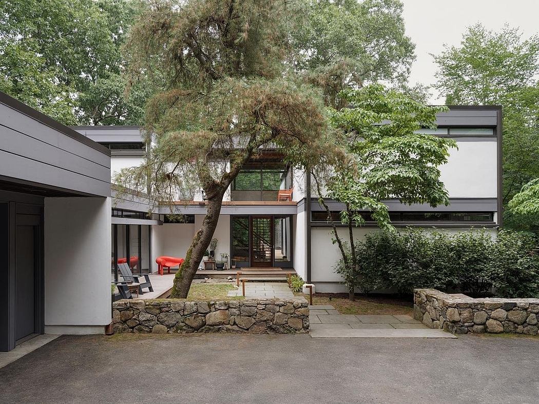 A modern, minimalist home with large windows, a stone exterior, and a lush tree canopy.