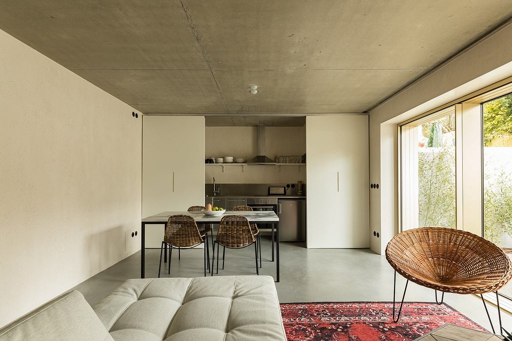 Contemporary open-plan kitchen and living area with concrete ceiling, large windows, and minimalist furniture.