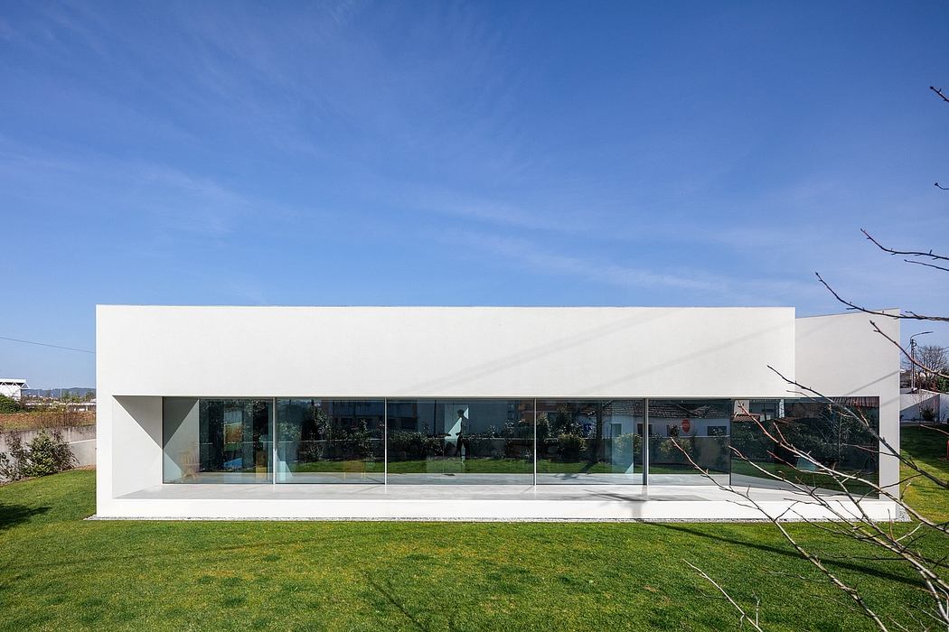 A minimalist, modern building with clean lines, large glass windows, and a grassy lawn.