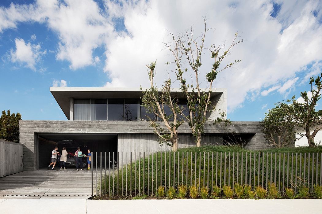 Concrete exterior with overhanging roof, glass walls, and mature trees surrounding the building.