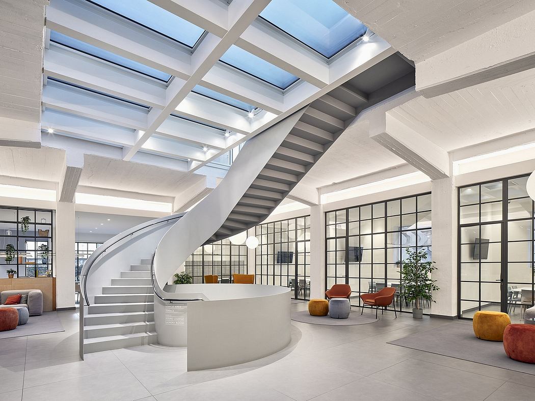 A modern, spacious lobby with a curved staircase, skylights, and cozy seating areas.