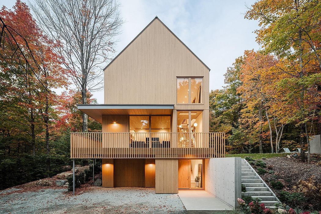 A modern two-story cabin with a wraparound porch and large windows overlooking a forested landscape.