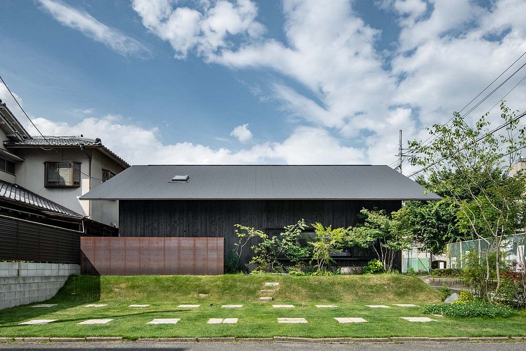 Modern Japanese-style home with black timber exterior, lush greenery, and paved walkway.