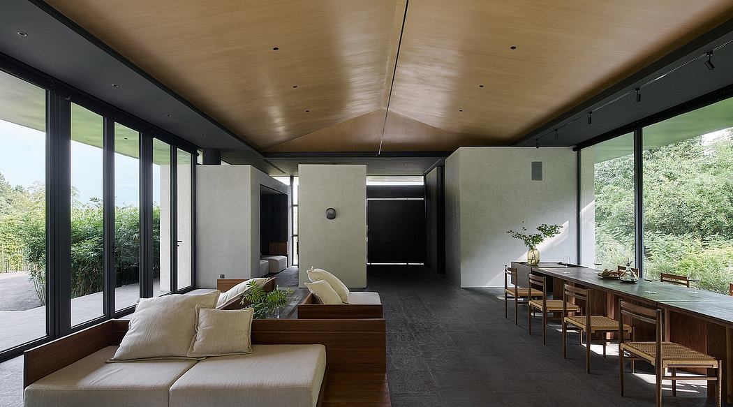 A modern, open-plan living space with floor-to-ceiling windows, wooden ceiling, and minimalist furnishings.