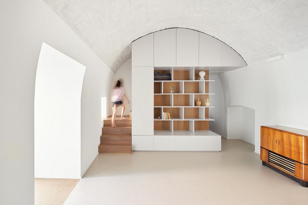 A modern, minimalist space with a curved shelving unit and wooden staircase.