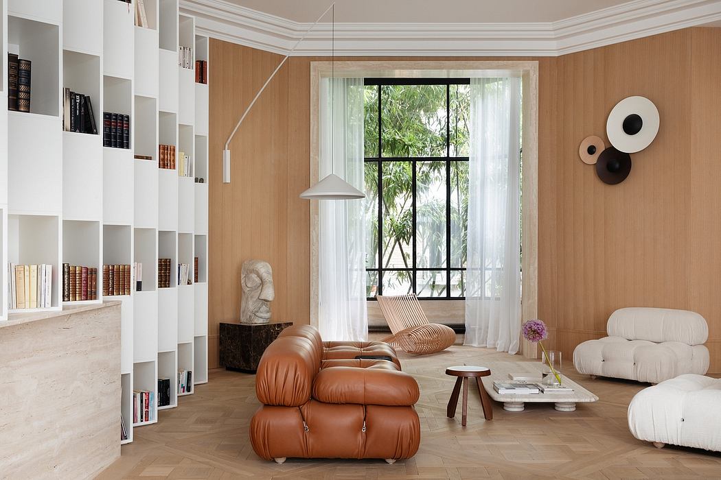 Spacious, minimalist living room with large window, wooden shelving, and plush leather seating.