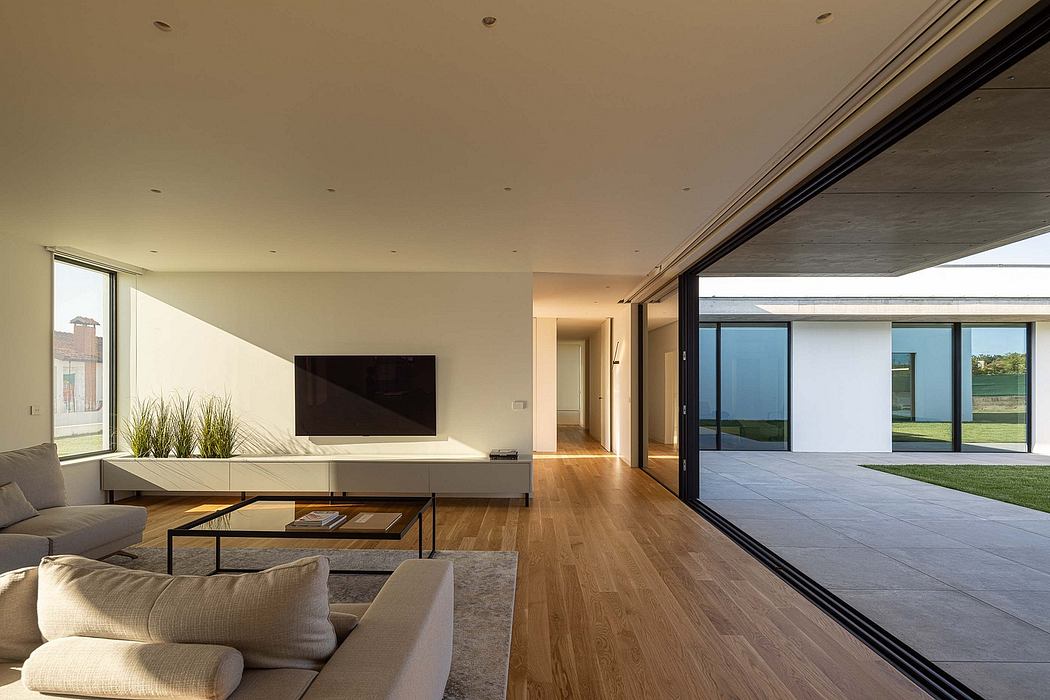 Modern, open-plan living space with wood flooring, minimalist furniture, and large glass windows overlooking the outdoors.