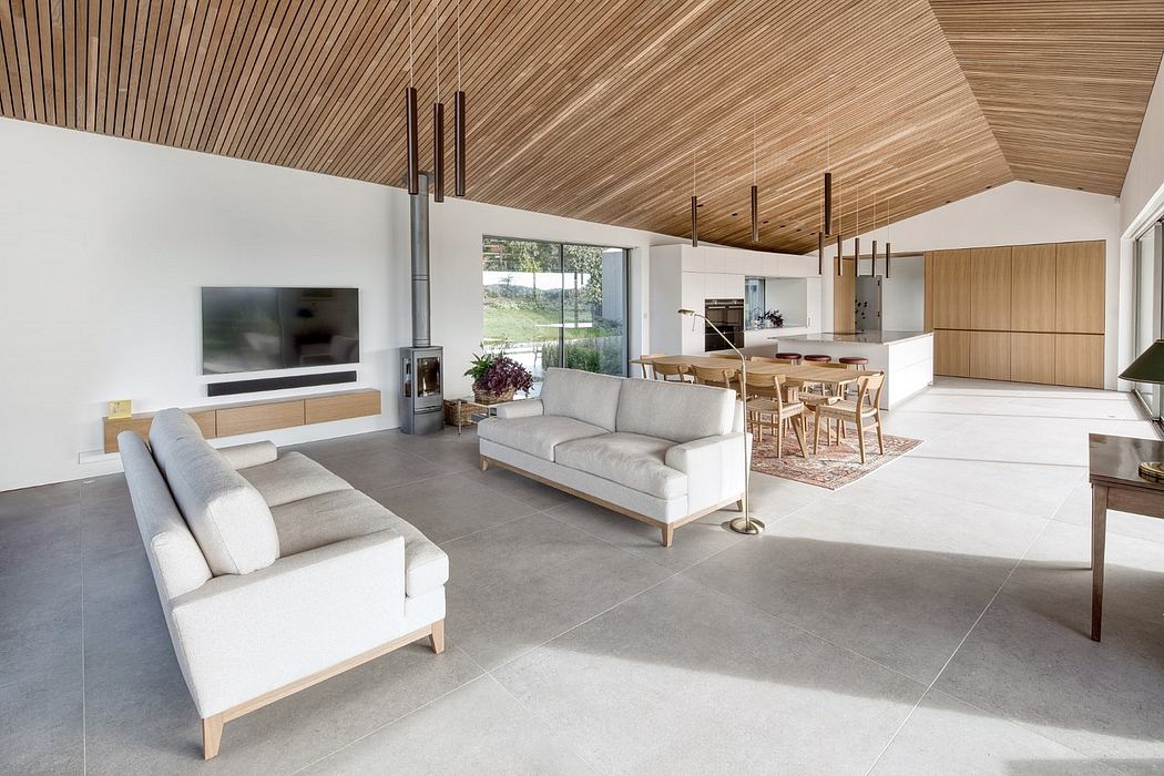 Spacious open-plan living area with modern wood-paneled ceiling, large windows, and minimalist furnishings.