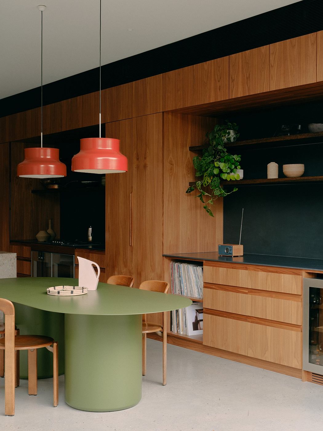 A modern kitchen with sleek wood panels, a green dining table, and contemporary red pendant lights.