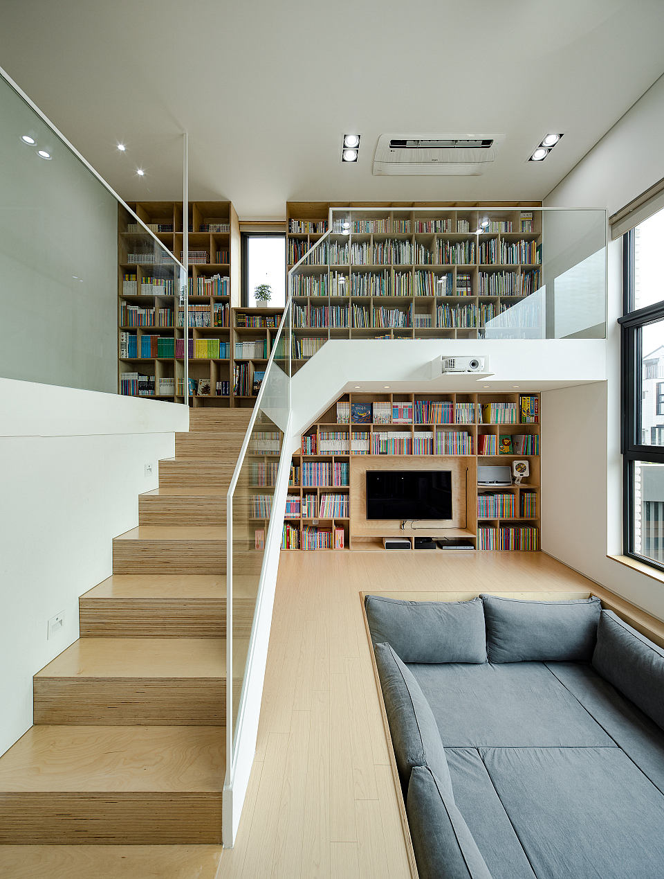 Spacious living room with wooden staircase, built-in bookshelves, and cozy gray sofa.