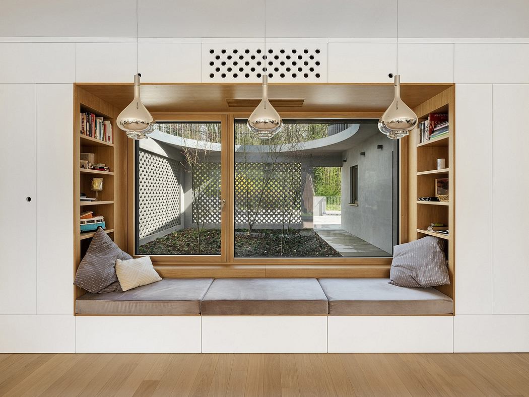 A modern living space with a cozy seating nook, bookshelves, and a view of an outdoor garden through large windows.