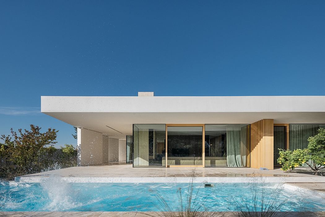 A sleek, modern house with large glass walls, a swimming pool, and a lush garden setting.