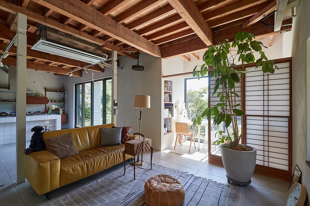 Warm, rustic living space with wooden ceiling beams, large windows, and lush greenery.