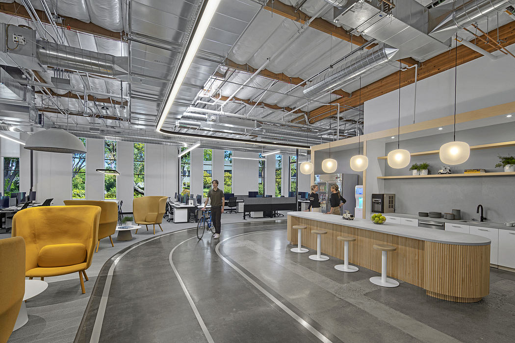 A modern, open-concept office space with a curved concrete floor, exposed ceiling, and warm wood accents.