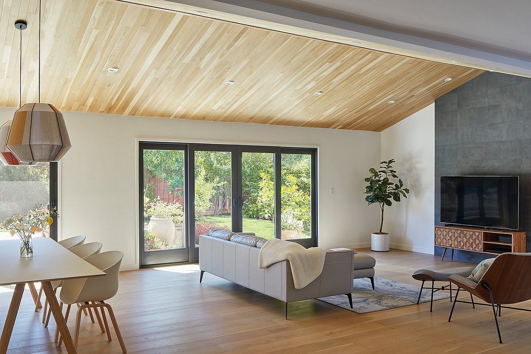 An open-concept living room with a wood-paneled ceiling, large windows, and modern furniture.