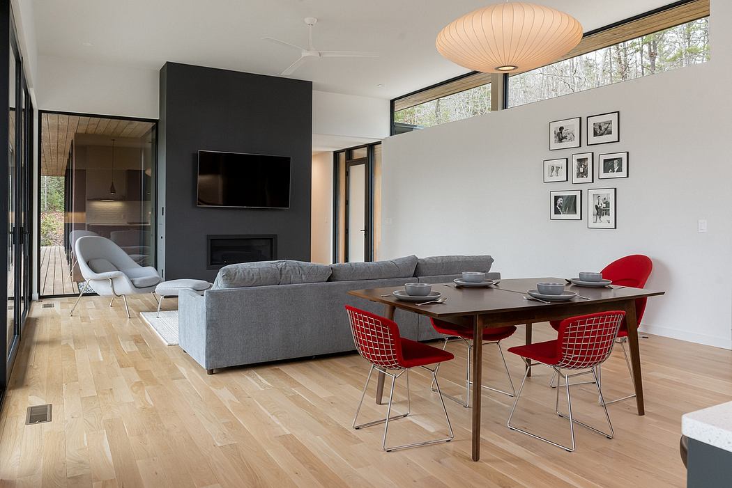 Modern, open-plan living space with a gray sofa, red dining chairs, and a large window overlooking nature.