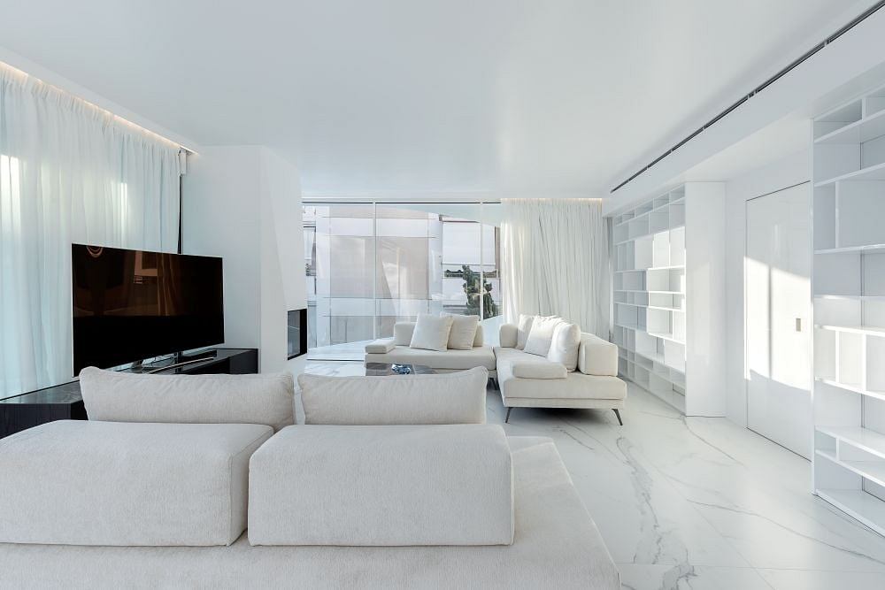 Sleek, modern living room with white furniture, marble flooring, and floor-to-ceiling windows.