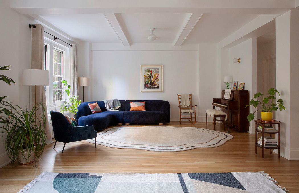 Spacious living room with plush blue sofa, armchair, and hardwood floors. Ornate framed artwork and potted plants accent the airy, modern design.