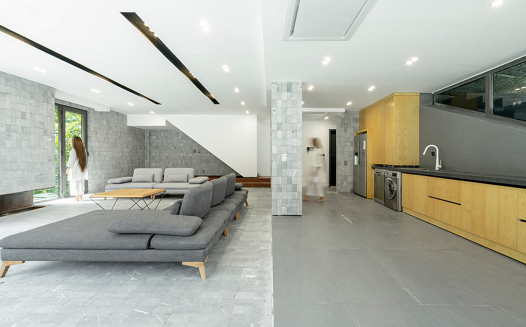 Spacious open-plan living area with modern, minimalist design; grey tiled flooring and wooden cabinetry.