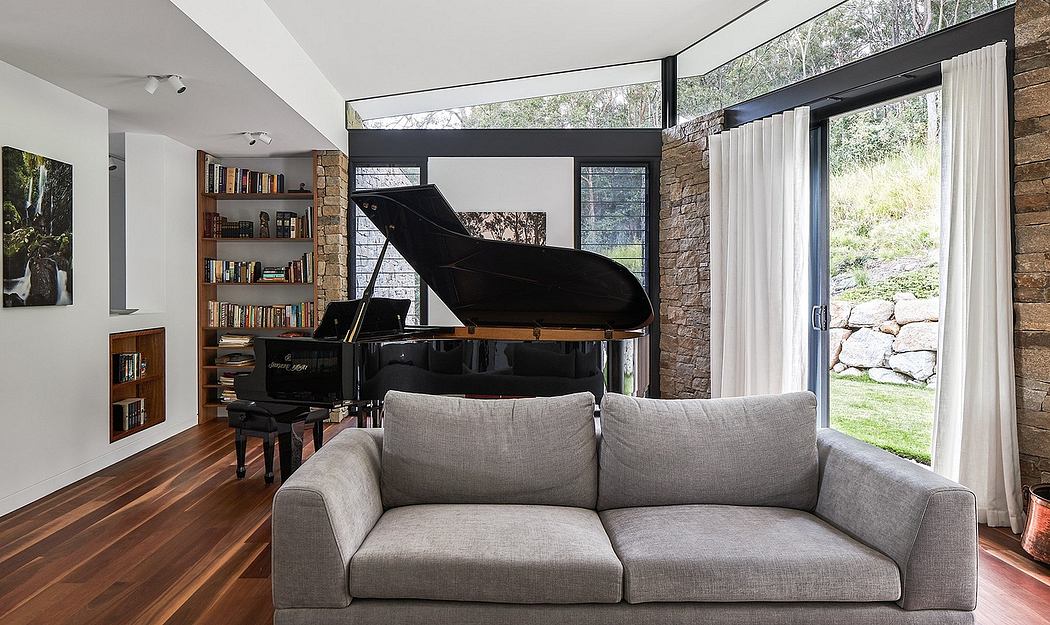 A modern and minimalist living room with a grand piano, cozy sofa, and large windows overlooking nature.