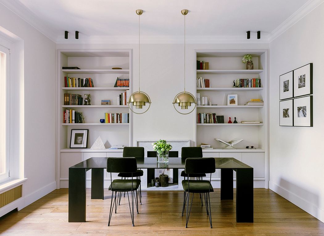 Minimalist dining room with built-in shelving, brass pendant lamps, and black dining chairs.
