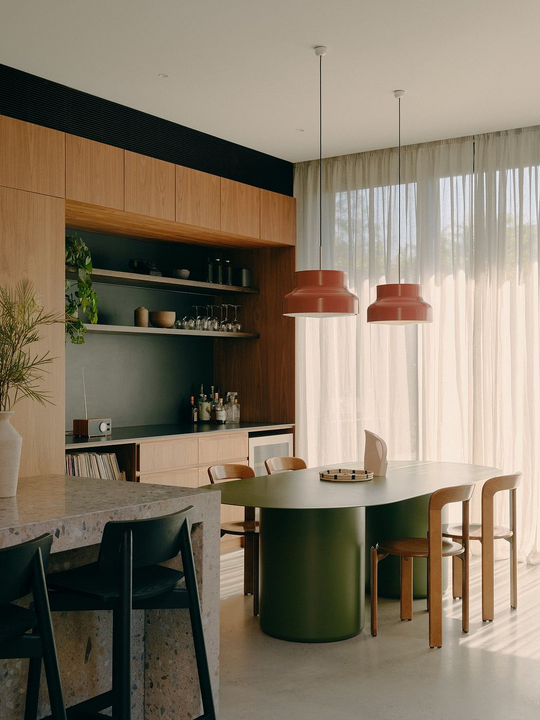 Sleek, modern kitchen design with open shelving, green table, and suspended red lamps.