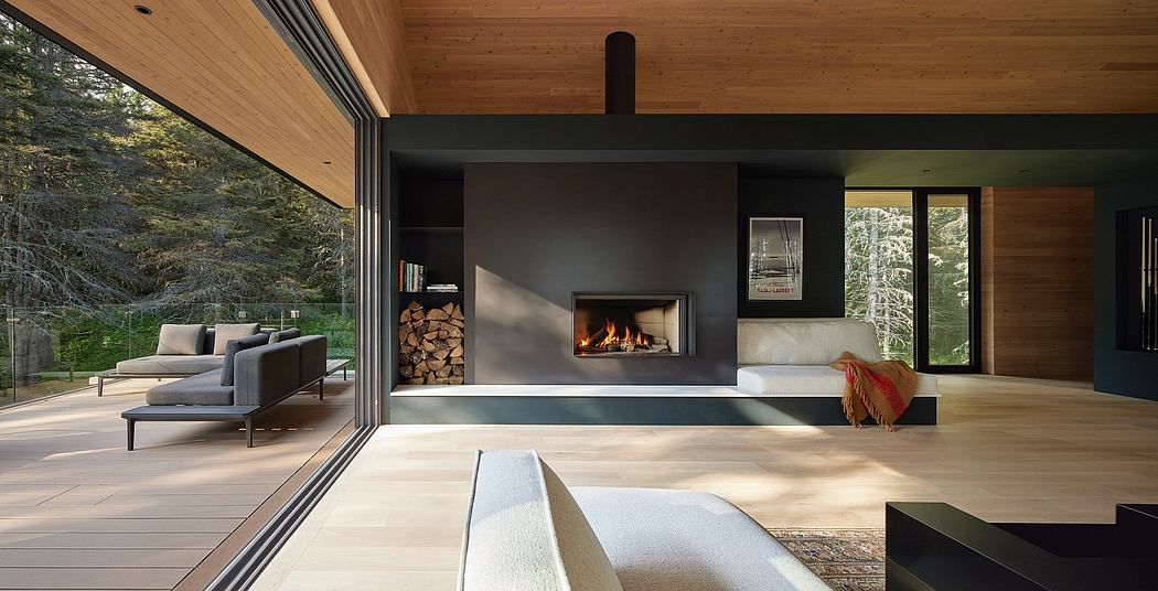 Cozy modern cabin with wood-paneled walls, large fireplace, and expansive windows overlooking the forest.