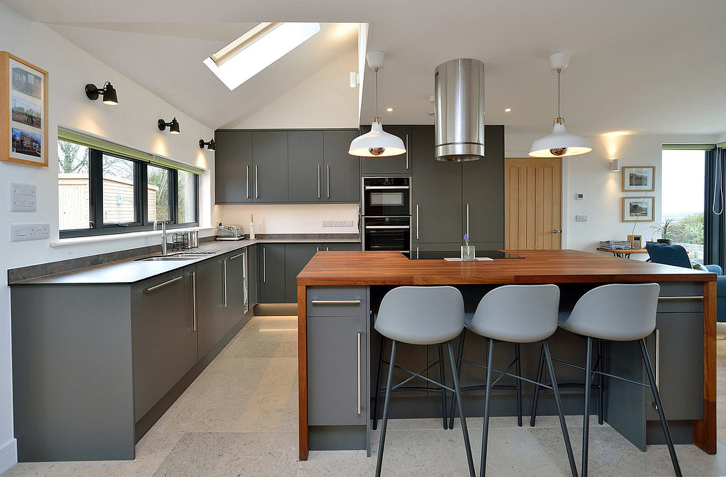A modern kitchen with sleek gray cabinets, wooden countertops, and pendant lighting.