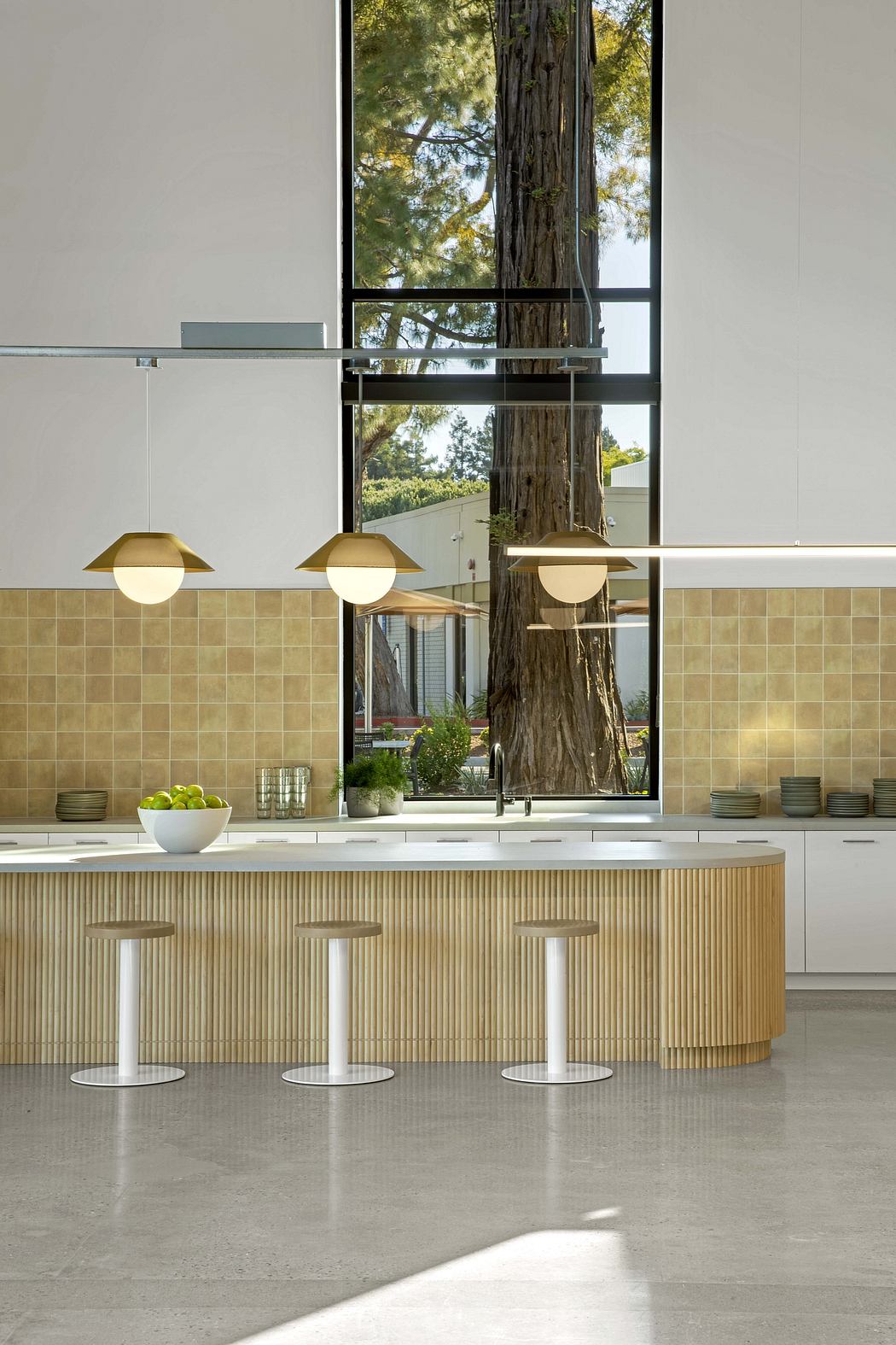 Minimalist kitchen design with wood-paneled island, pendant lights, and large window overlooking trees.