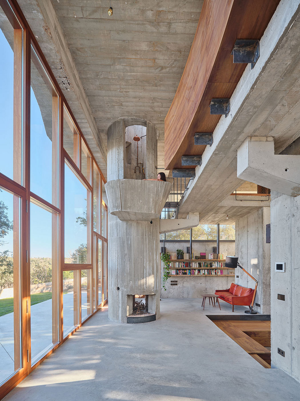 Striking concrete and wood interior with a curved archway, bookshelves, and a red sofa.