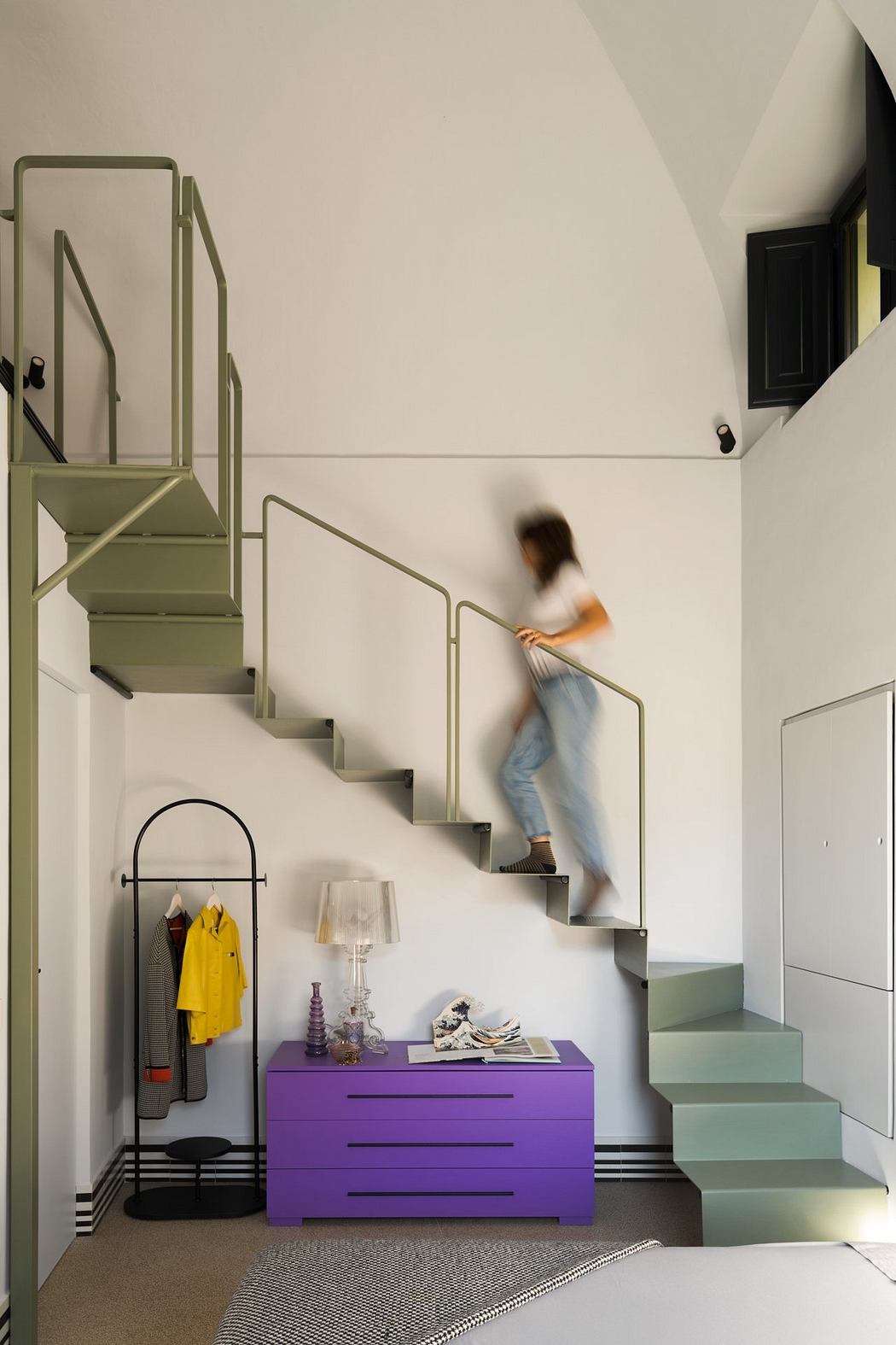 Striking staircase design with vibrant purple dresser and modern fixtures. Blurred figure ascending stairs.