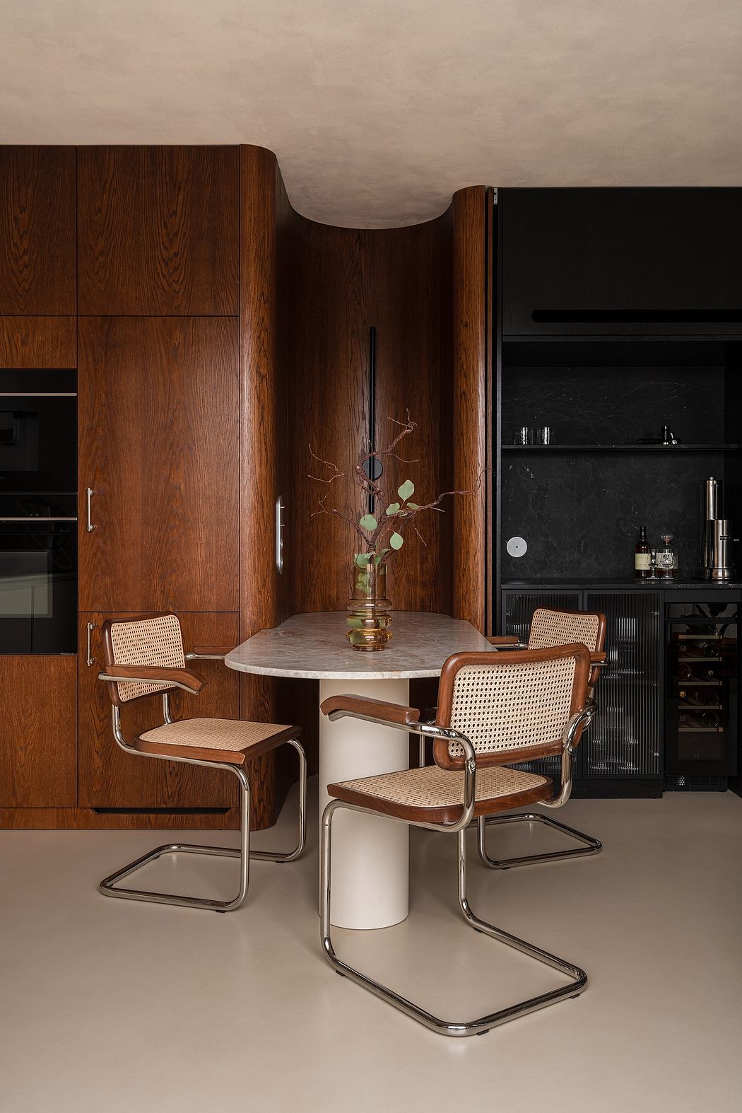 Warm-toned wooden cabinetry, sleek chrome chairs, and a sculptural floral centerpiece.