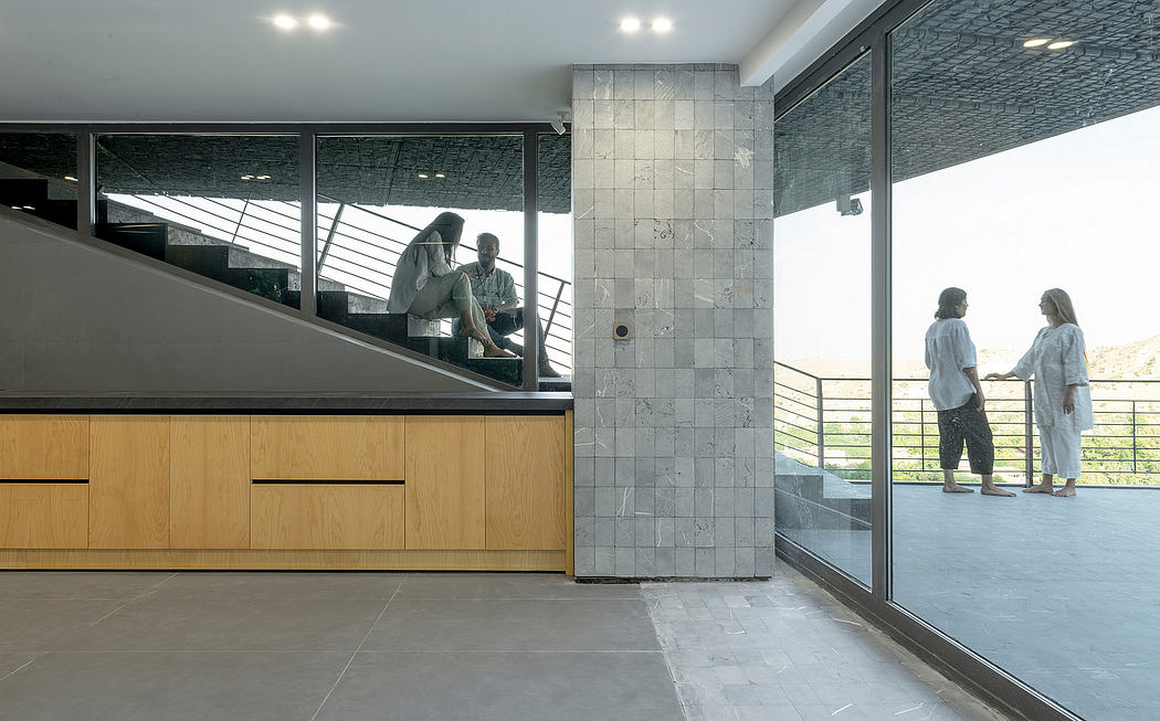 A modern interior with grey tiles, wooden cabinetry, and floor-to-ceiling windows overlooking a scenic view.