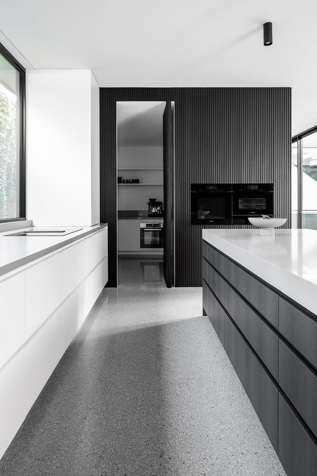 Sleek, minimalist kitchen with black vertical panels, built-in appliances, and terrazzo flooring.