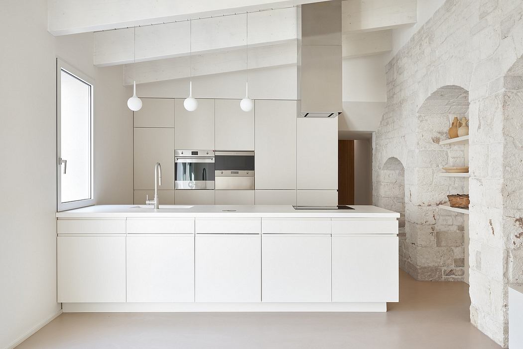 A modern, minimalist kitchen with clean lines, sleek white cabinets, and a rustic stone accent wall.