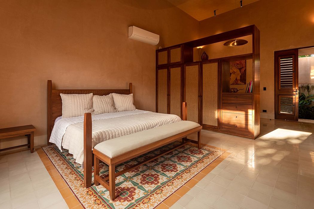 Warm-toned bedroom with wooden furnishings, intricate patterned rug, and a wall-mounted air conditioning unit.